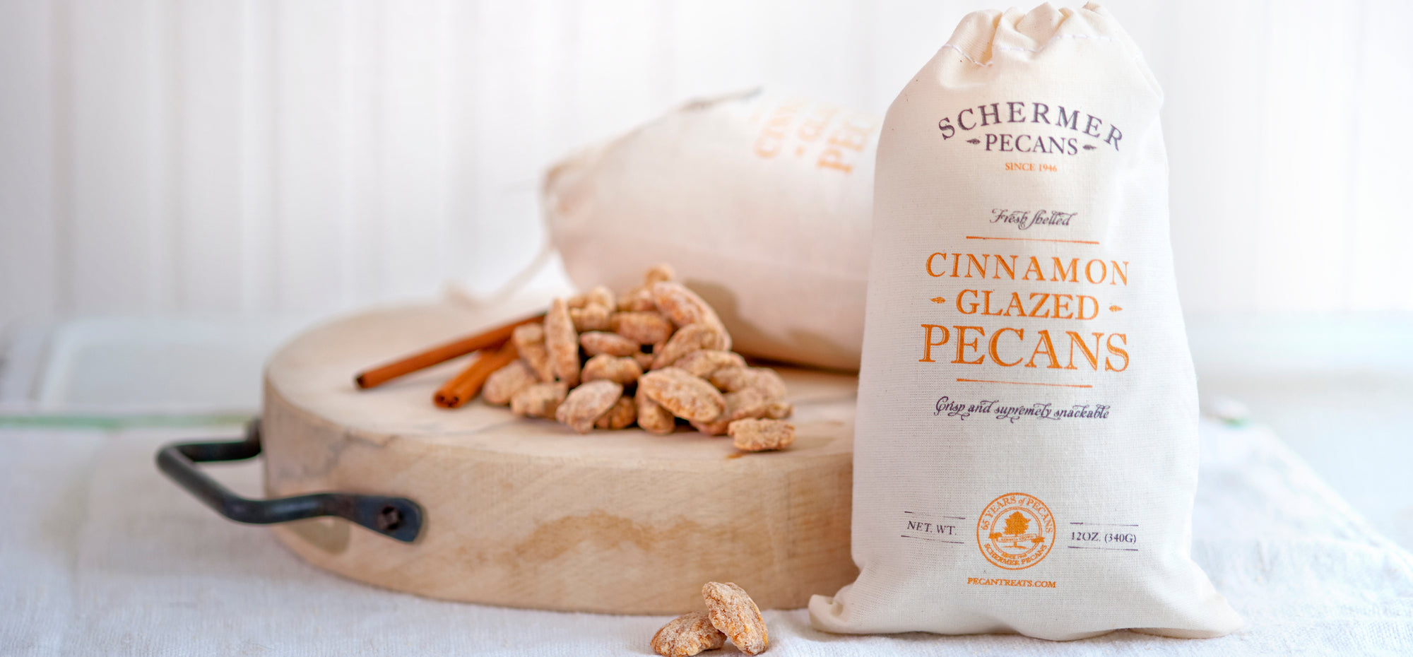 Image of Schermer Cinnamon Glazed Pecans in a cloth gift bag next to a cutting board with cinnamon glazed pecans and cinnamon sticks.